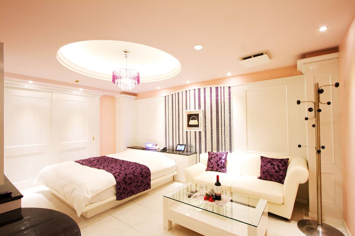A hotel room with two beds, a glass coffee table, a white sofa, a chandelier, and a wall-mounted coat rack.