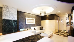 Une chambre d’hôtel moderne avec un grand lit, un canapé blanc, une table basse en verre et un lustre.