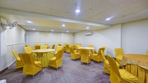 Une salle de conférence avec des chaises et des tables jaunes, des murs blancs et un ventilateur de plafond.