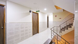 Un couloir d’hôtel avec une porte en bois, un panneau indiquant la sortie de secours et un escalier doté de rampes en métal.