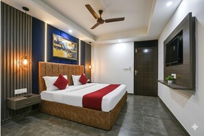 Une chambre d’hôtel moderne dotée d’un grand lit, d’un ventilateur de plafond, d’un téléviseur fixé au mur et d’une étagère murale agrémentée d’une plante.