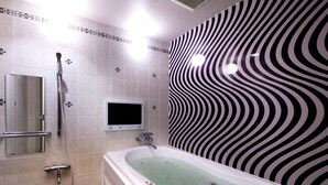 A modern bathroom with a bathtub, a handheld shower, a toilet, and a wall-mounted TV. - Hotel Baron -the Sweet Modern - Adults Only (Togo)