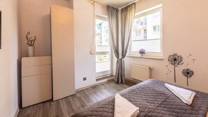 A bedroom with a bed, a small table, a radiator, and a window with curtains. - Victus Apartamenty - Bella (Sopot)