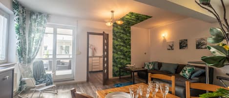 A dining area with a wooden table set for four, a sofa, and a wall with a green leafy pattern.