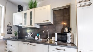 A modern kitchen with white cabinets, a stainless steel sink, and a microwave. - Victus Apartamenty - Bella (Sopot)
