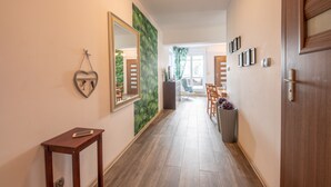 A hallway with a wooden floor, a heart-shaped mirror, a small table, and a green wall mural. - Victus Apartamenty - Bella (Sopot)