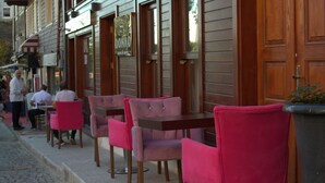 A row of pink chairs and tables outside a building with wooden doors and windows. - Qonaq Hotel (Istanbul)