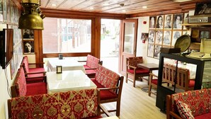 A restaurant with red upholstered booths and a glass table, wooden ceiling, and framed pictures on the walls. - Qonaq Hotel (Istanbul)