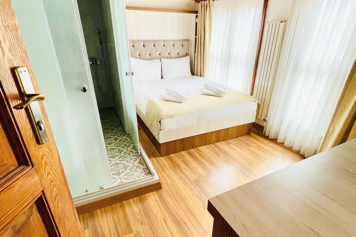 Ein Schlafzimmer mit Holzboden, einem Bett mit weißen Leinen, einem Holztisch und einer Tür zu einem Badezimmer.