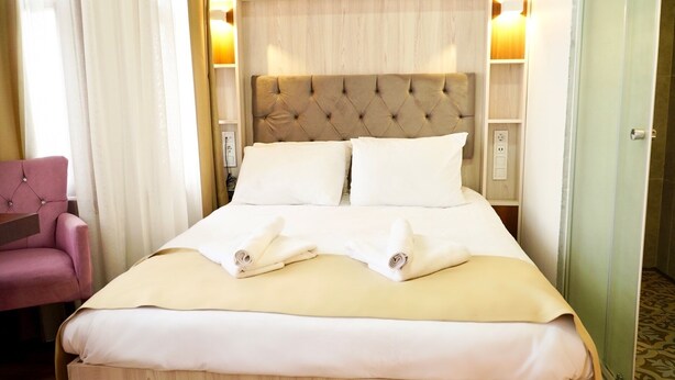 A hotel room with a large bed, a pink armchair, and a wooden headboard. - Qonaq Hotel (Istanbul)
