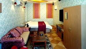 A hotel room with a bed, a sofa, a small table with glasses, a wooden wardrobe, and patterned wallpaper.