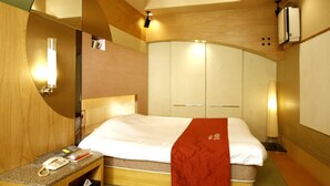 A hotel room with a bed, a bedside telephone, a mirror, and a wall-mounted air conditioning unit.