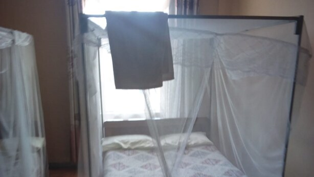 A single bed with a mosquito net, a wooden floor, and a chair.
