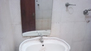 A bathroom with a white pedestal sink, a wooden door, and a mirror above the sink.