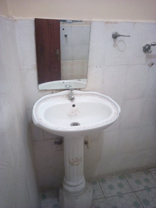 Un baño con un lavamanos blanco de pedestal, una puerta de madera y un espejo sobre el lavamanos.