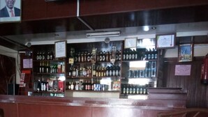 A bar area with a polished wooden counter and shelves stocked with various bottles.