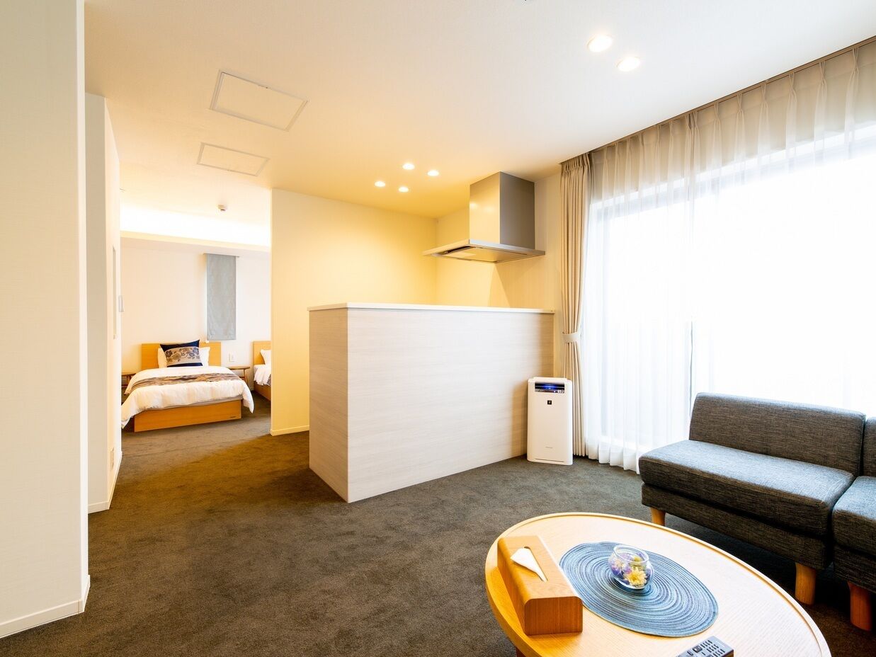 A hotel room with a bed, a sofa, a small table, a desk, and a window with curtains.