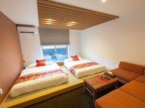 Habitació d'hotel amb dos llits, un sofà, una taula petita i una finestra amb vistes.