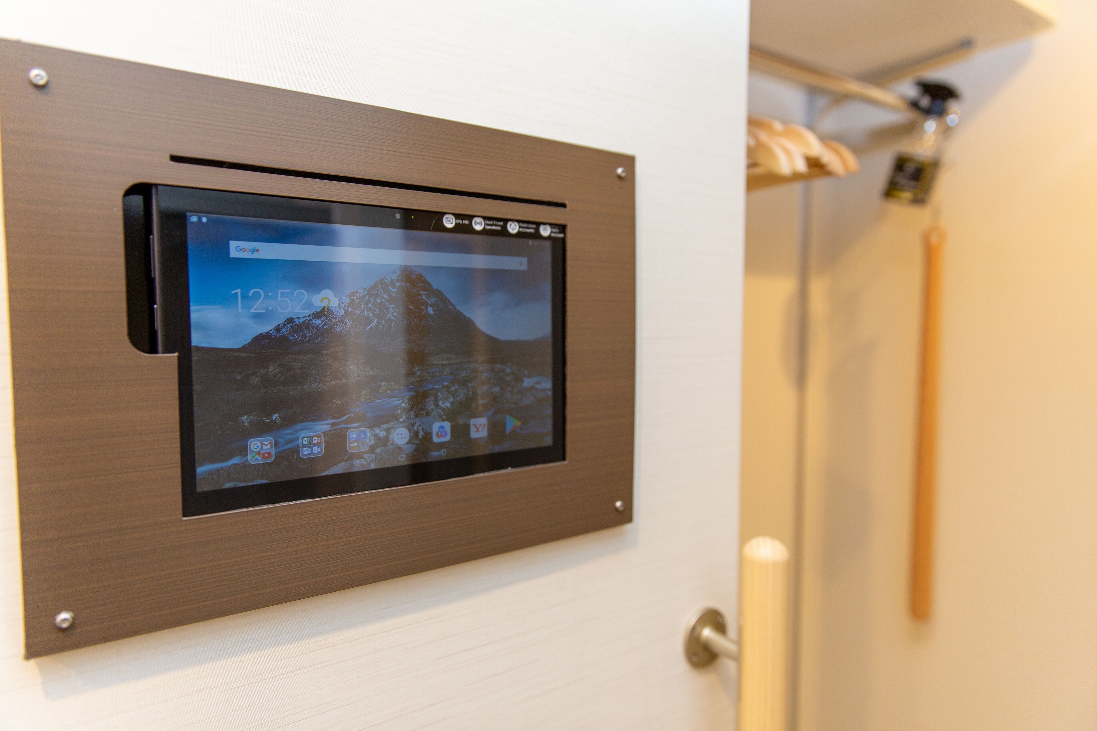 A digital display mounted on a door, showing a mountain landscape and time as 12:52.