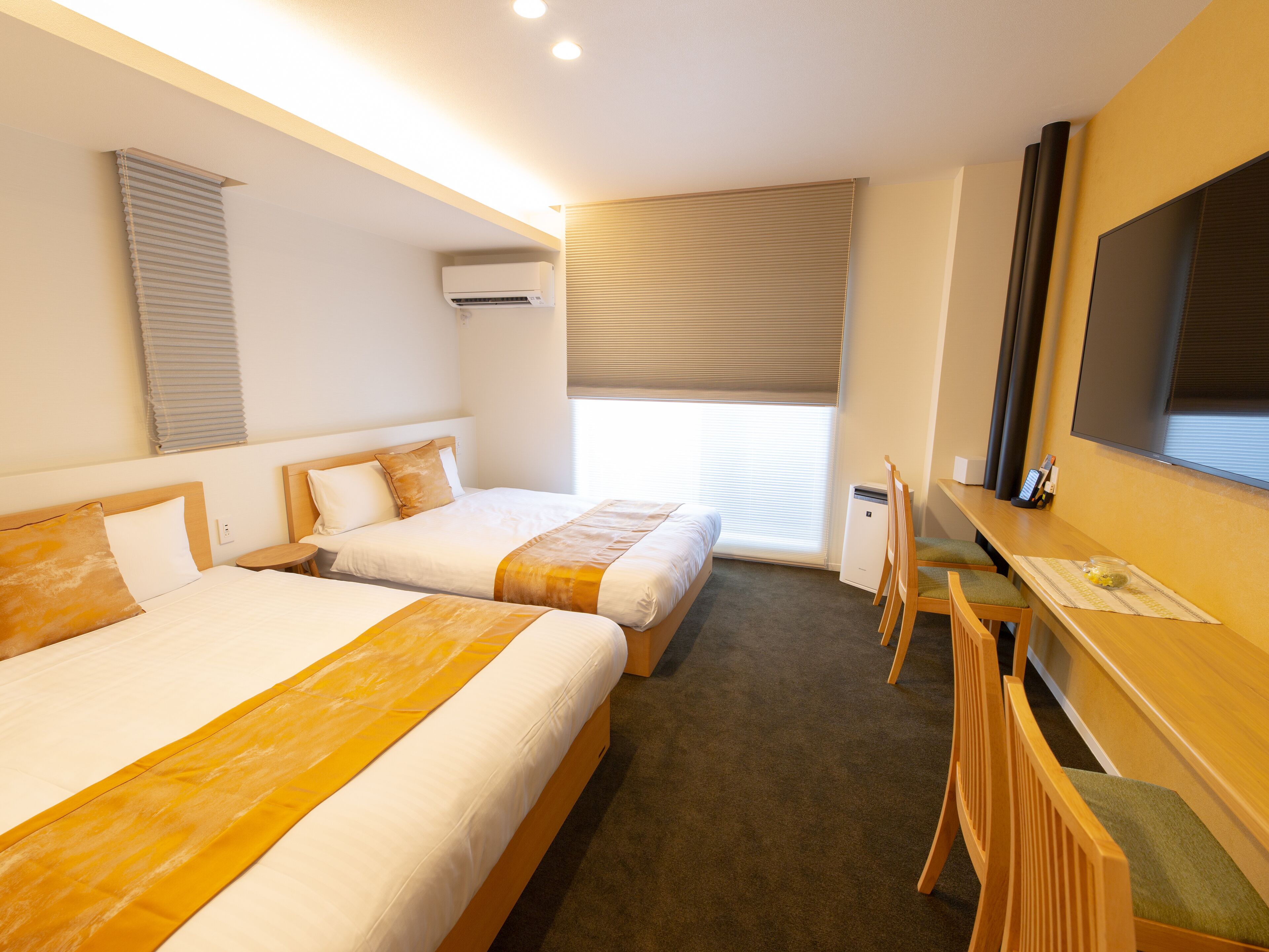 A hotel room with two beds, a desk with a chair, a TV, and a window with blinds.