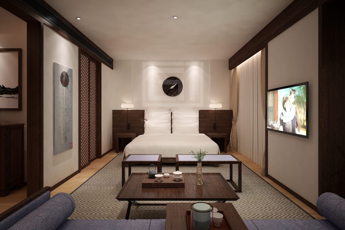 A modern hotel room with a large bed, a TV, a coffee table with a vase and teapot, and a sofa.