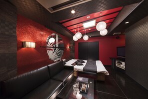 A modern room with a red accent wall, a black leather sofa, a bed with a white headboard, and a small table with glasses and a decorative item. - Hotel Baron Club -one DAY Resort - Adults Only (Okazaki)