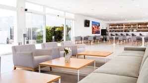 Un moderno vestíbulo de hotel con área de descanso, un bar y amplias ventanas que ofrecen vistas a zonas verdes.