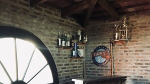 Un coin bar rustique avec une grande roue en bois, des tabourets en bois, un comptoir et un mur de briques orné d’étagères où sont disposées des bouteilles.