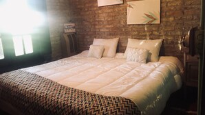 Une chambre avec un mur en briques, un grand lit recouvert de linge de lit blanc et deux tableaux encadrés accrochés au mur.