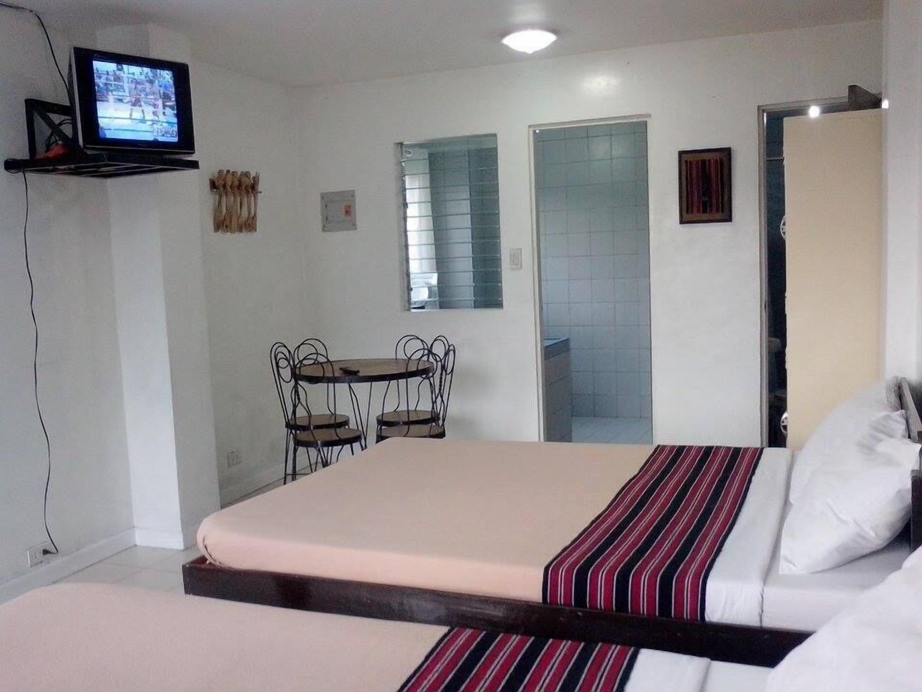 A hotel room with a bed, a small table with chairs, a television on a stand, and a door.