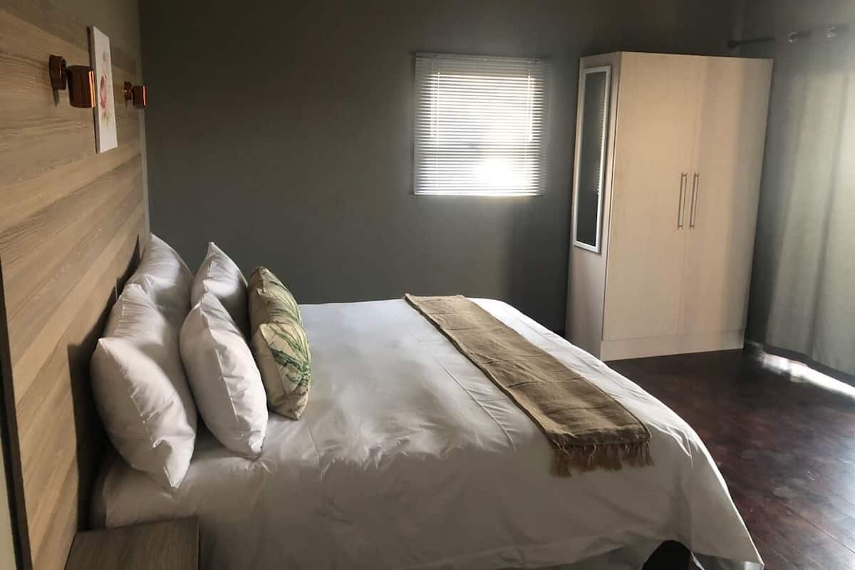 A bedroom with a bed, pillows, a blanket, a wardrobe, and a window with blinds.