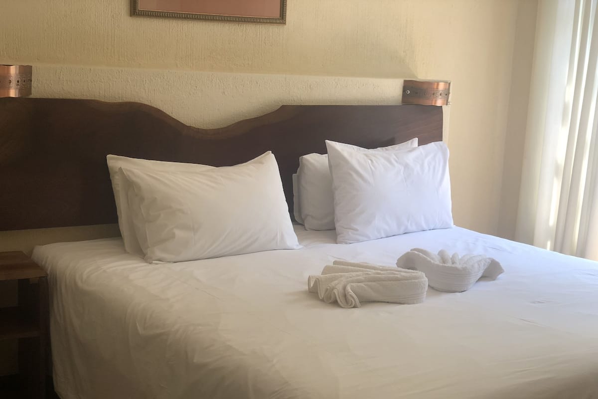 A neatly made bed with white linens and pillows, a wooden headboard, and a set of towels on the bed.