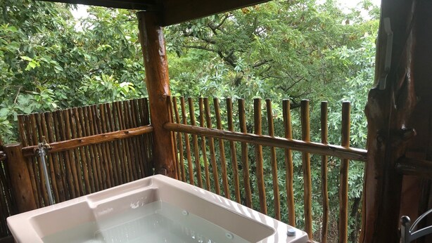 Un bain à remous sur une terrasse en bois, avec une clôture en bambou et une végétation luxuriante en arrière-plan.