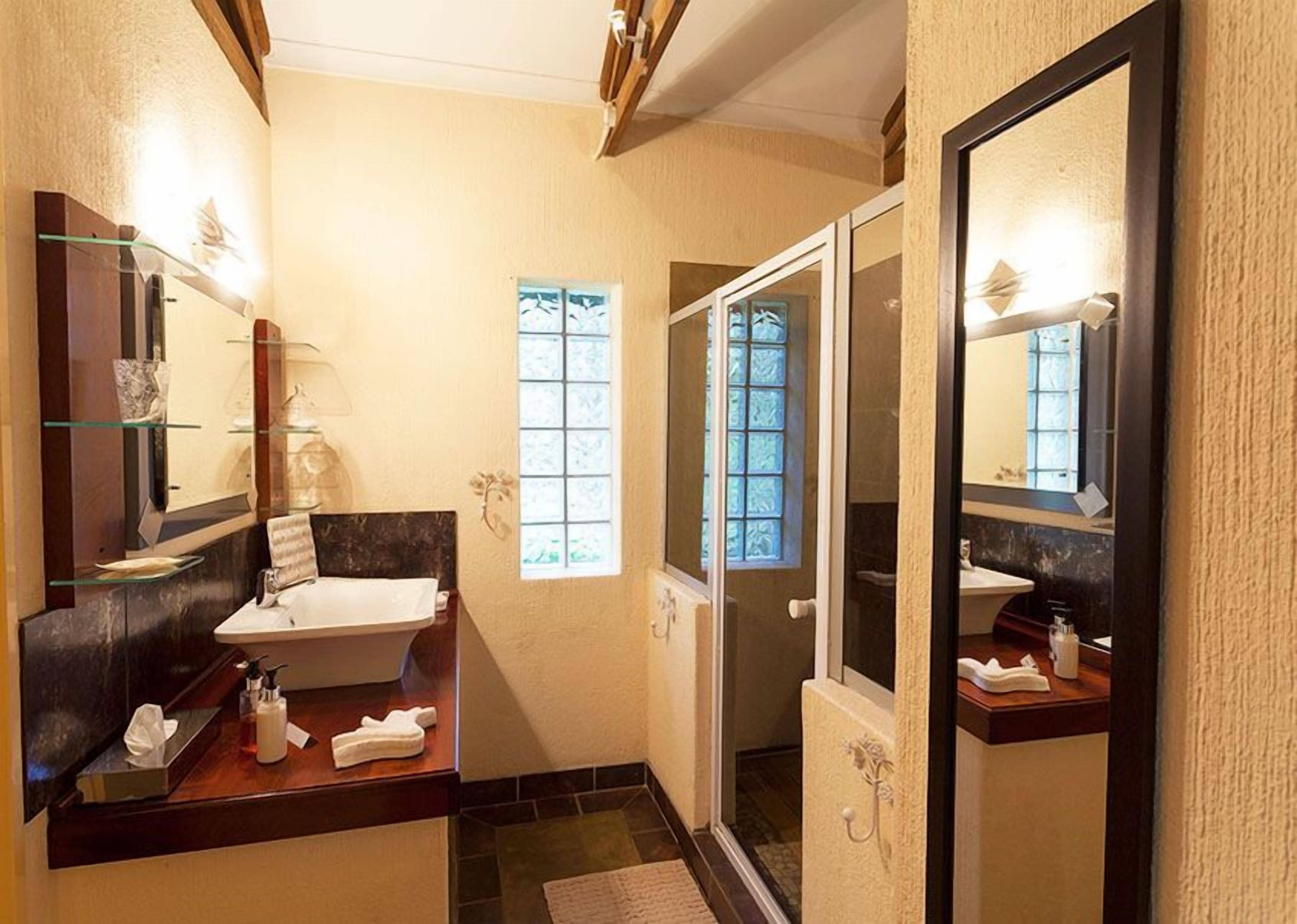 A bathroom with a vanity, a large mirror, a shower area, and a window providing natural light.