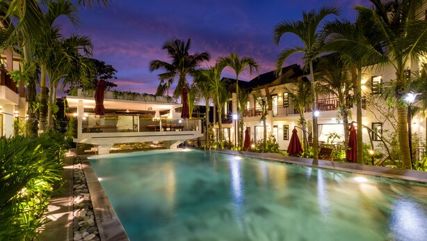 A pool area with a clear view of the pool, surrounding palm trees, and a building with multiple levels and outdoor seating. - Melica Resort & Spa Phu Quoc (Phu Quoc)