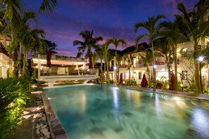 A pool area with a clear view of the pool, surrounding palm trees, and a building with multiple levels and outdoor seating. - Melica Resort & Spa Phu Quoc (Phu Quoc)