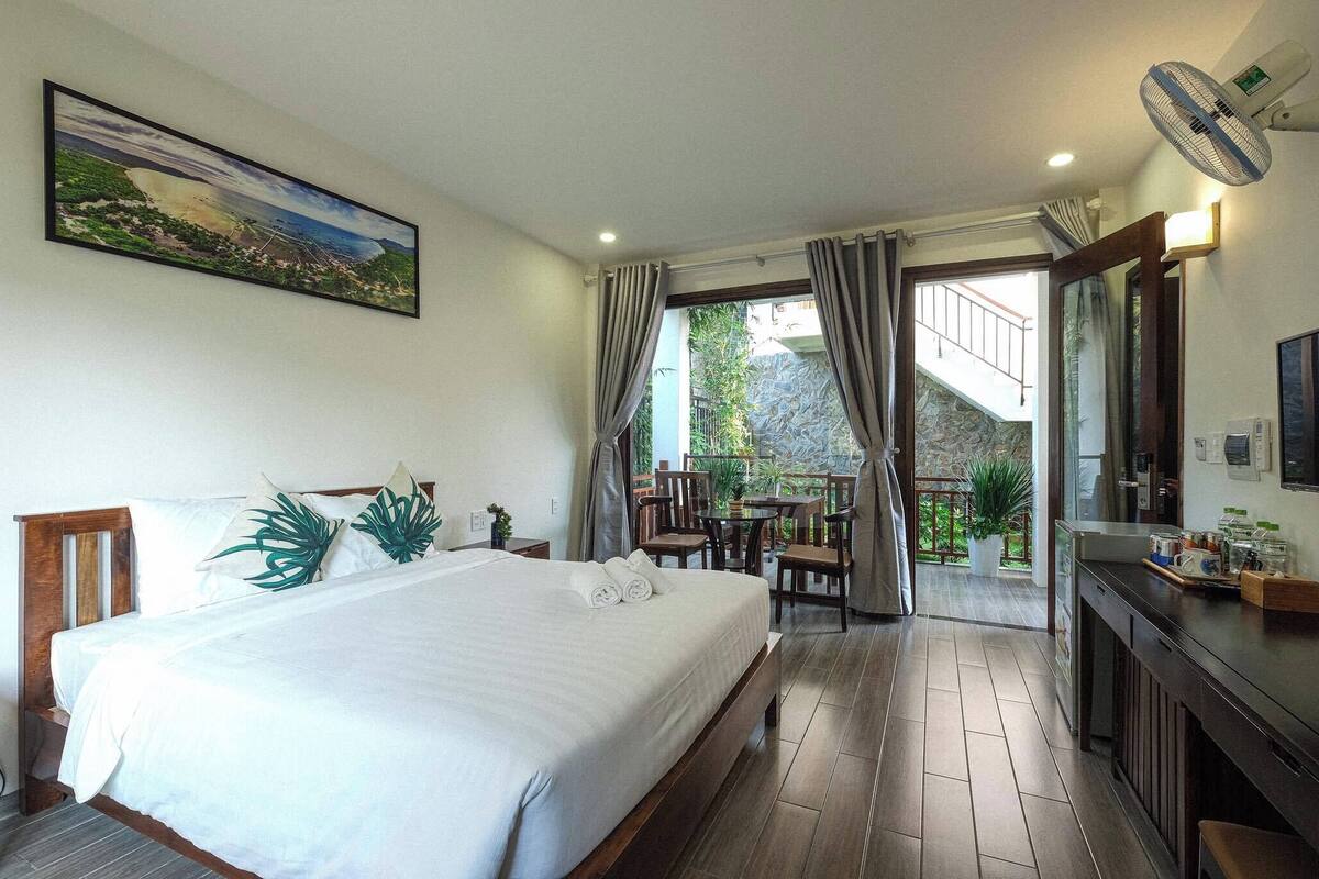 A hotel room with a large bed, a dining area, and a view of the outdoors.