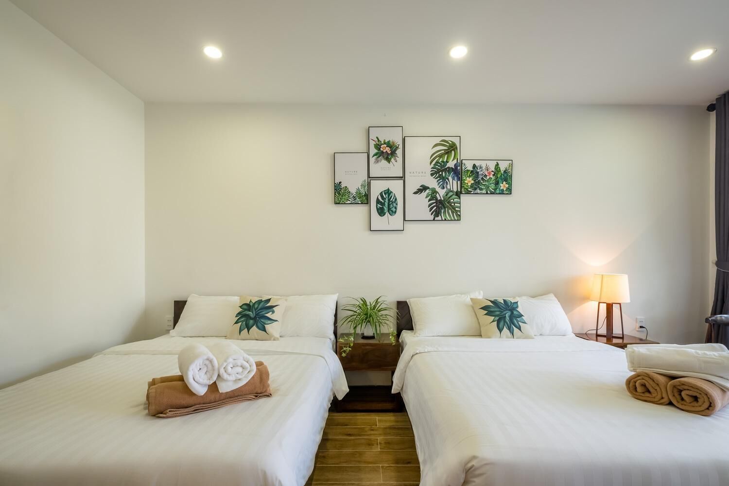 Ein Hotelzimmer mit zwei Betten, einer Wand mit gerahmten Bildern von Naturmotiven, einem Nachttisch mit Lampe und einem kleinen Topfpflanzen.