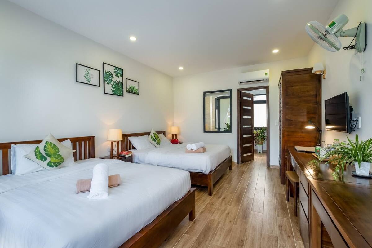 A hotel room with two beds, a wooden dresser, a desk, a TV, and a bathroom visible through an open door.