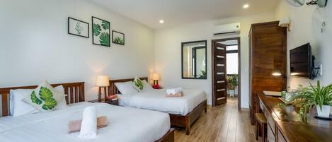 A hotel room with two beds, a wooden dresser, a desk, a TV, and a bathroom visible through an open door.