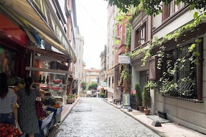 A narrow cobblestone street with a fruit stand on the left and a building with a sign for 'Unique Suites' on the right. - Gorgeous Two Bedroom Apartment in Taksim - 3AC (Istanbul)