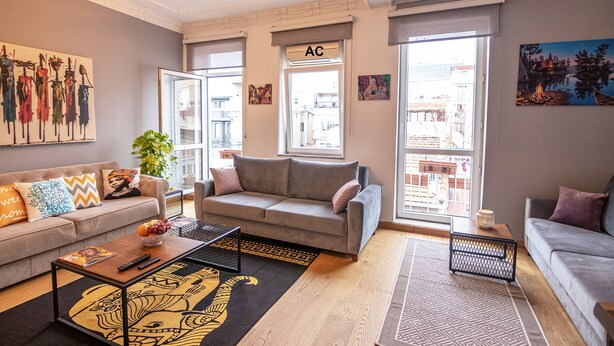 A living room with a grey sofa, a coffee table, and a patterned rug. There is a window with an air conditioning unit labeled 'AC'. - Gorgeous Two Bedroom Apartment in Taksim - 3AC (Istanbul)