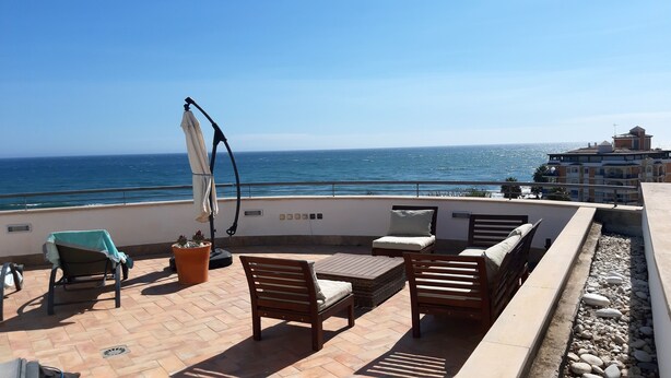 Une terrasse avec des meubles d’extérieur, une plante en pot et une vue sur la mer.