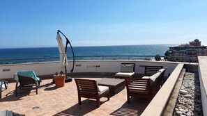 Une terrasse avec des meubles d’extérieur, une plante en pot et une vue sur la mer.