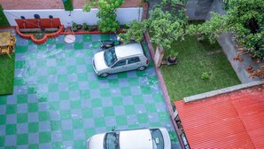 A rooftop parking area with two cars parked, surrounded by greenery and a red roof. - Silu Homes (Lalitpur)