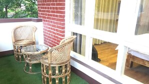 Wicker furniture on a green artificial lawn, a brick wall, and a window with curtains. - Silu Homes (Lalitpur)