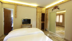 A bedroom with a bed, a television on a wooden stand, and a sliding door leading to another room. - Silu Homes (Lalitpur)
