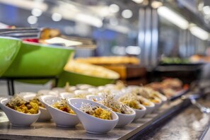 A buffet line with various dishes in white bowls, including a green container and a tray with bread. - Gran Sagitario (Ciutadella de Menorca)