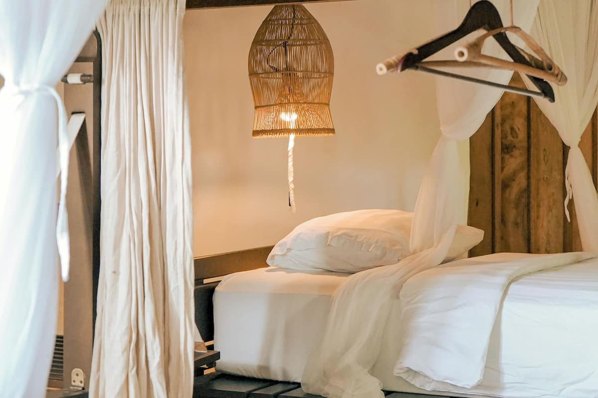 A bed with white bedding, a hanging light fixture, and a wooden ceiling.