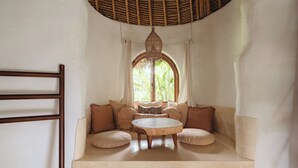 A cozy seating area with a round wooden table, cushioned benches, and a hanging light fixture. - Mana Earthly Paradise (Ubud)